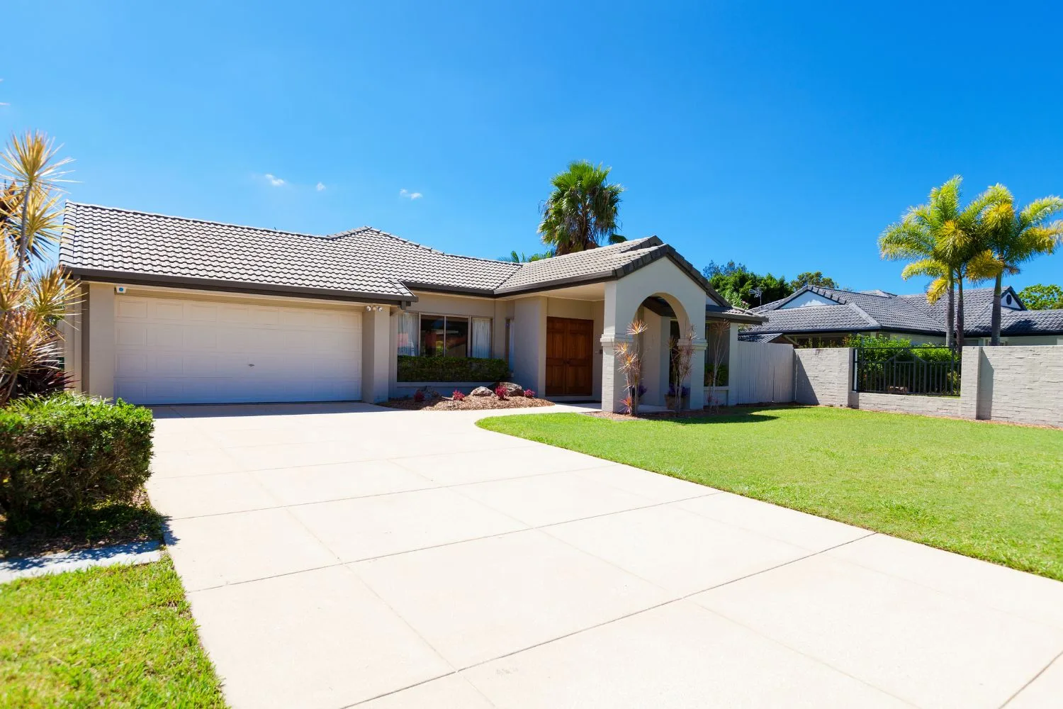Wide plain concrete driveway curving past a lawn to a double garage
