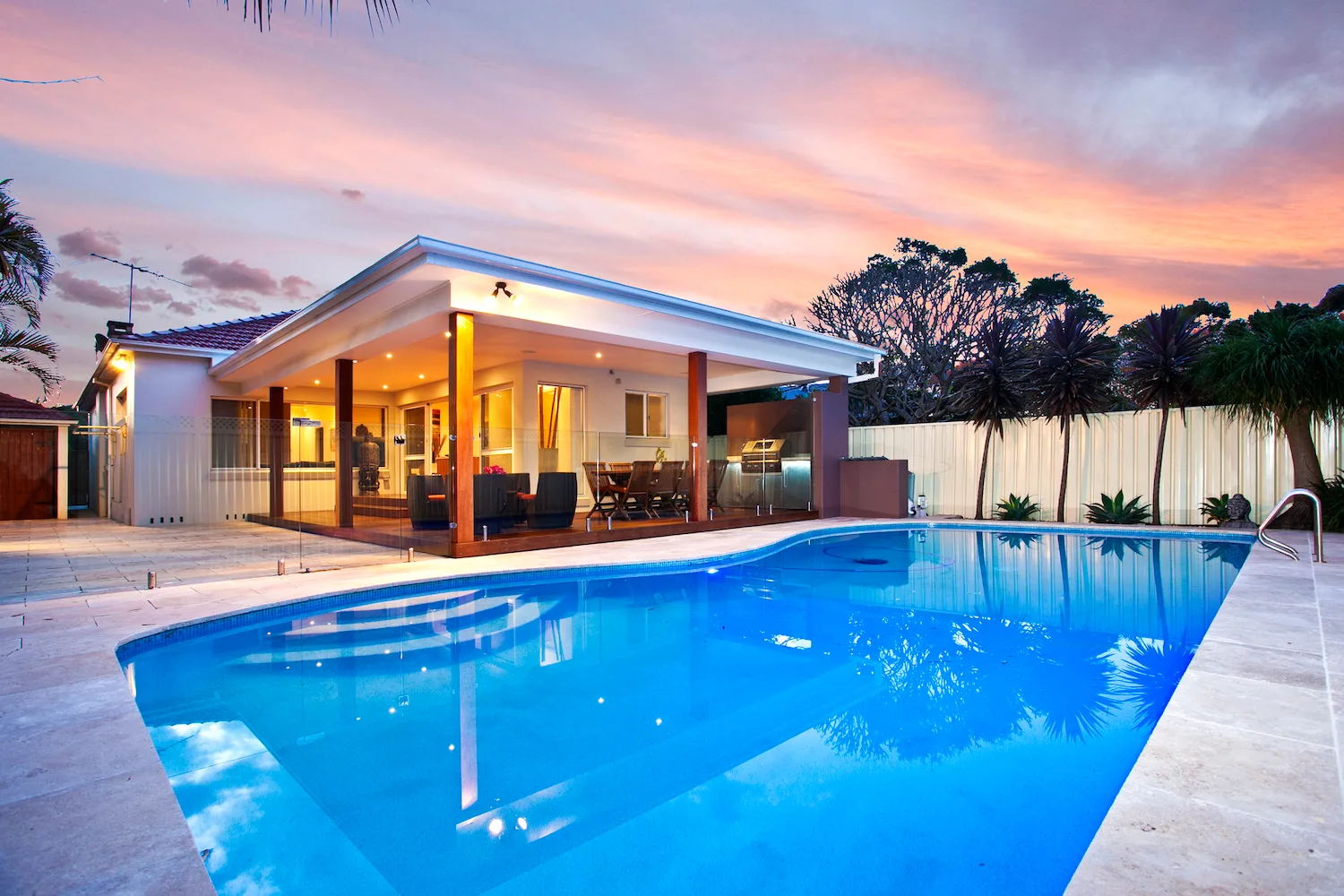 Concrete pool surround beside an inground pool and alfresco area at dusk